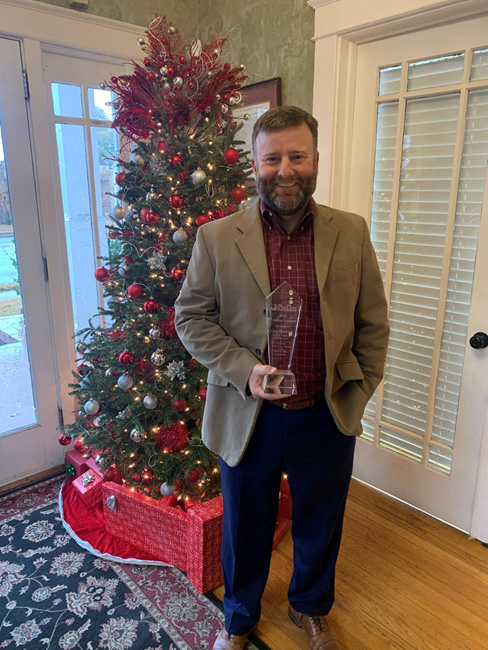 Greg posing with President's Award by the Christmas tree
